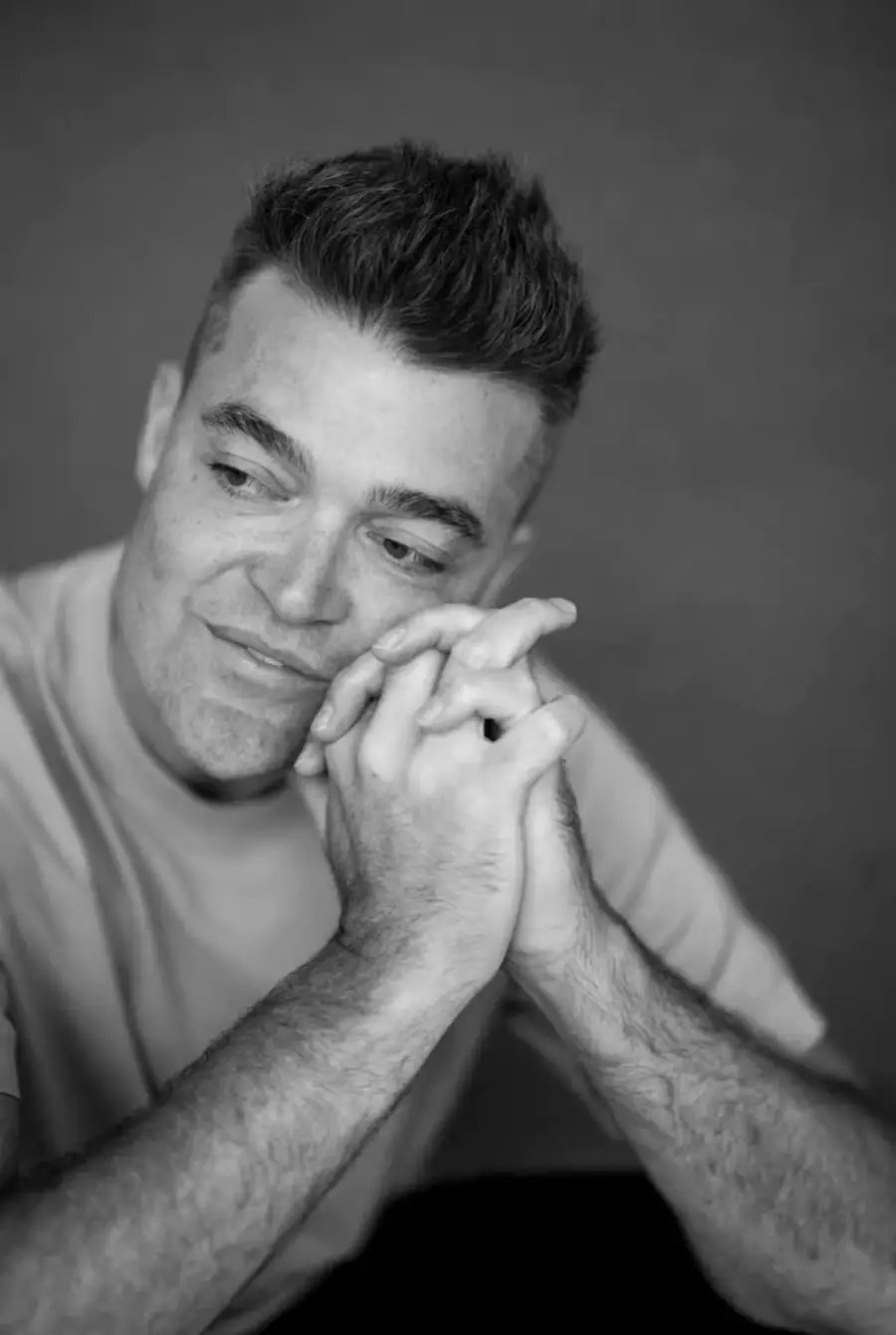 Nathan Morris, hands together, looks up and smiles.